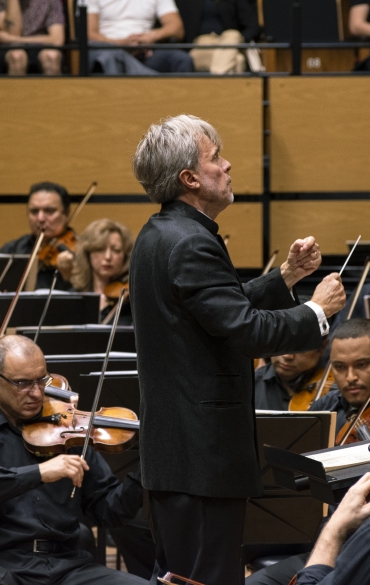 Maestro Pawet Przytocki com orquestra ao fundo.