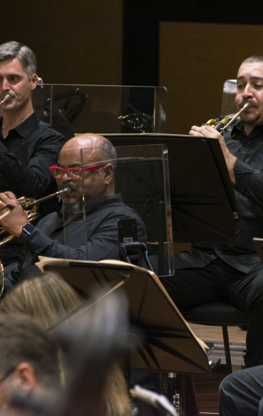 Vemos músicos da orquestra tocando instrumentos de sopro.