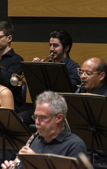 Vemos músicos da orquestra tocando instrumentos de sopro.