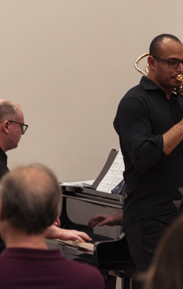 Vemos o trombonista José Milton Vieira tocando e atrás dele o pianista Paulo Bergmann.