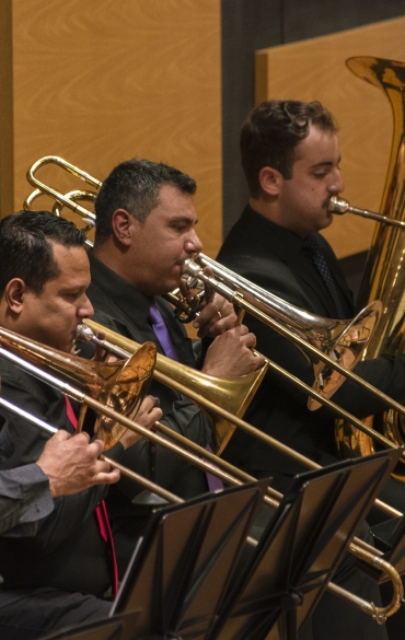 Vemos quatro músicos enfileirados, da esquerda para a direita. Os três primeiros deles, da esquerda para a direita, tocam trompete e o último, o mais longe da câmera, toca tuba.