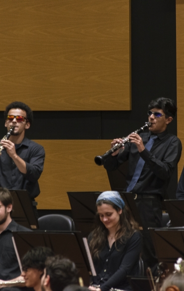 Vemos dois meninos tocando clarinete. Ambos usam óculos de sol coloridos, laranja e roxo.