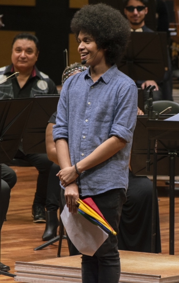 Vemos, no centro da imagem, o mestre de cerimônias Oséas Duarte. Ele está sorrindo, com os braços abaixados. Ele segura um mini guarda chuva colorido.