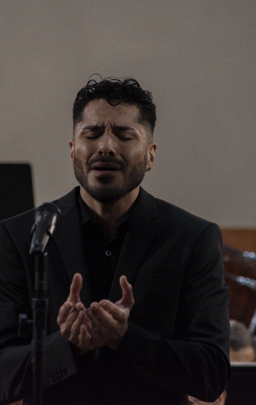 Vemos o solista Matías Herrera cantando, ele junta as duas mãos à frente do corpo. Ele está de olhos fechados.