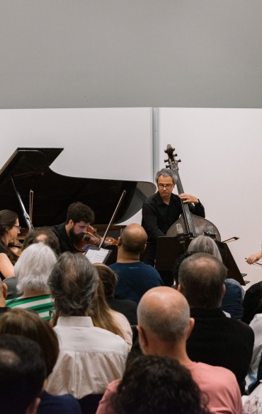 Na imagem, aparece o público e ao fundo, no centro, cinco músicos: a pianista Olinda Allessandrini e quatro músicos do naipe de cordas, Brigitta Calloni (violino), João Senna (viola), Martina Ströher (violoncelo) e Luciano Dal Molin (contrabaixo). 