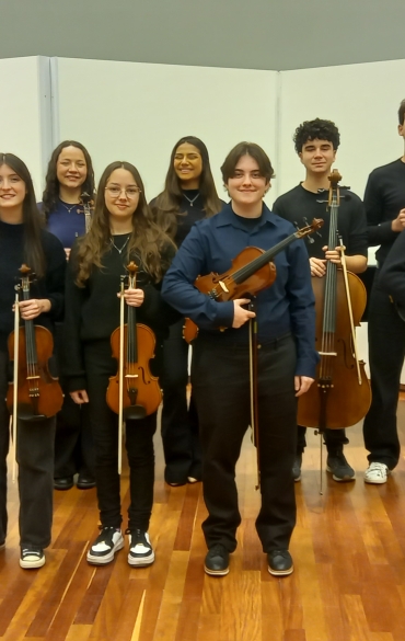 Jovens alunos da escola da ospa com instrumentos posam em sala com parede branca e ch&atilde;o de madeira
